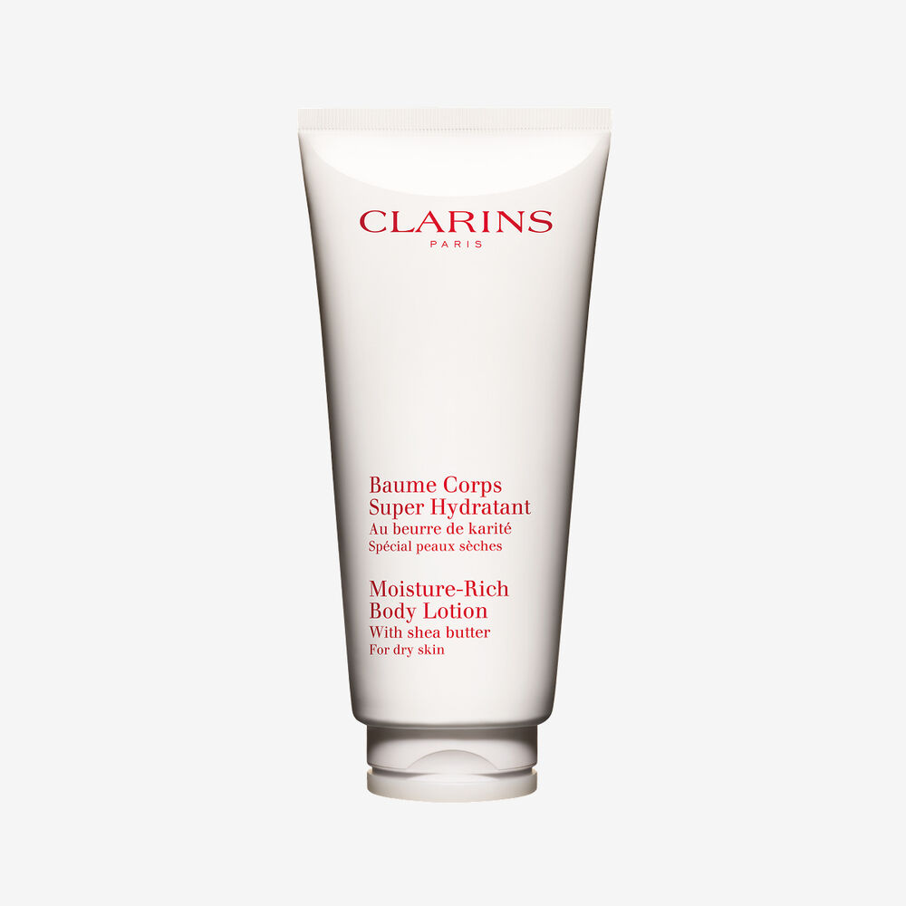Packshot of a tube of Clarins Moisture-Rich Body Lotion by Clarins close to some shea nuts on a white background.