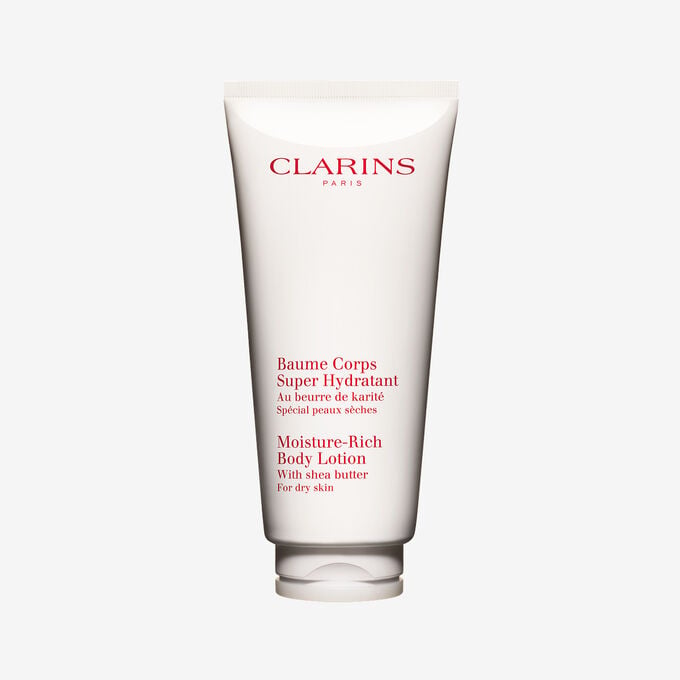 Packshot of a tube of Clarins Moisture-Rich Body Lotion by Clarins close to some shea nuts on a white background.
