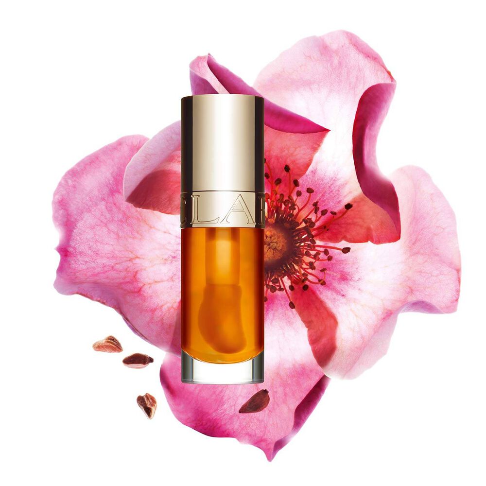 Packshot of Clarins Lip Comfort Oil in Honey, placed next to a sweetbriar rose on a light peach background.