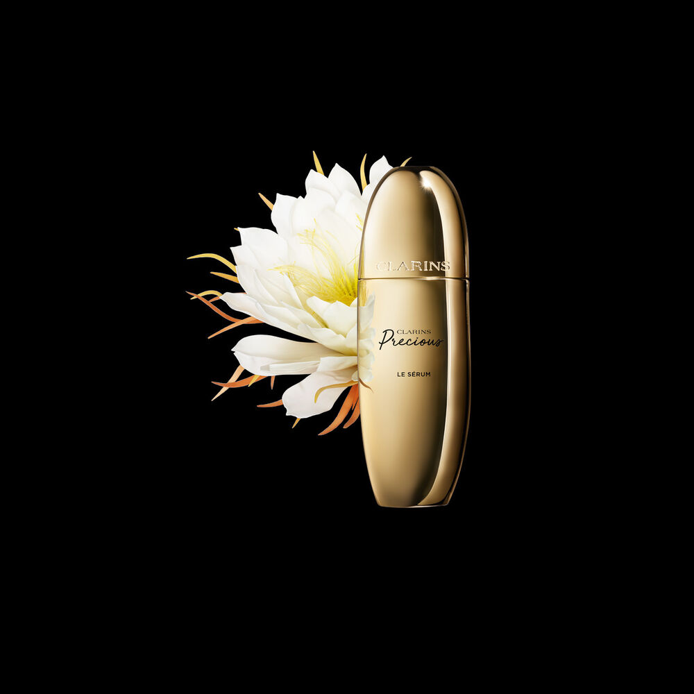 Packshot of Clarins Precious Serum close to a Moonlight flower on a dark background.