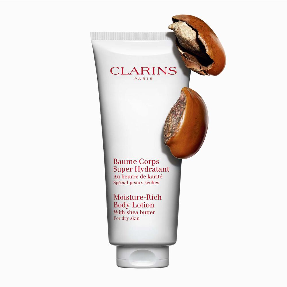 Packshot of a tube of Clarins Moisture-Rich Body Lotion by Clarins close to some shea nuts on a white background.