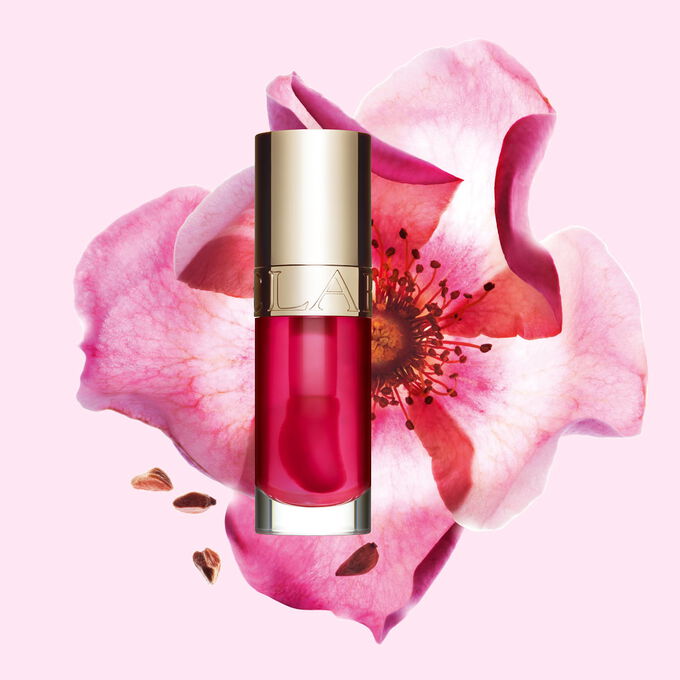 Packshot of Clarins Lip Comfort Oil in Pitaya, placed next to a sweetbriar rose on a light pink background.