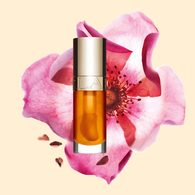 Packshot of Clarins Lip Comfort Oil in Honey, placed next to a sweetbriar rose on a light peach background.