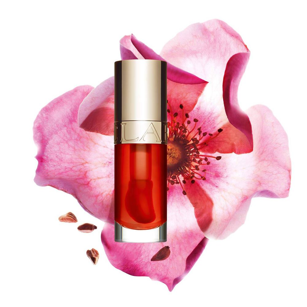 Packshot of Clarins Lip Comfort Oil Apricot, placed next to a sweetbriar rose on a light orange peach background.