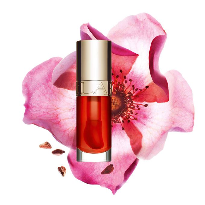 Packshot of Clarins Lip Comfort Oil Apricot, placed next to a sweetbriar rose on a light orange peach background.