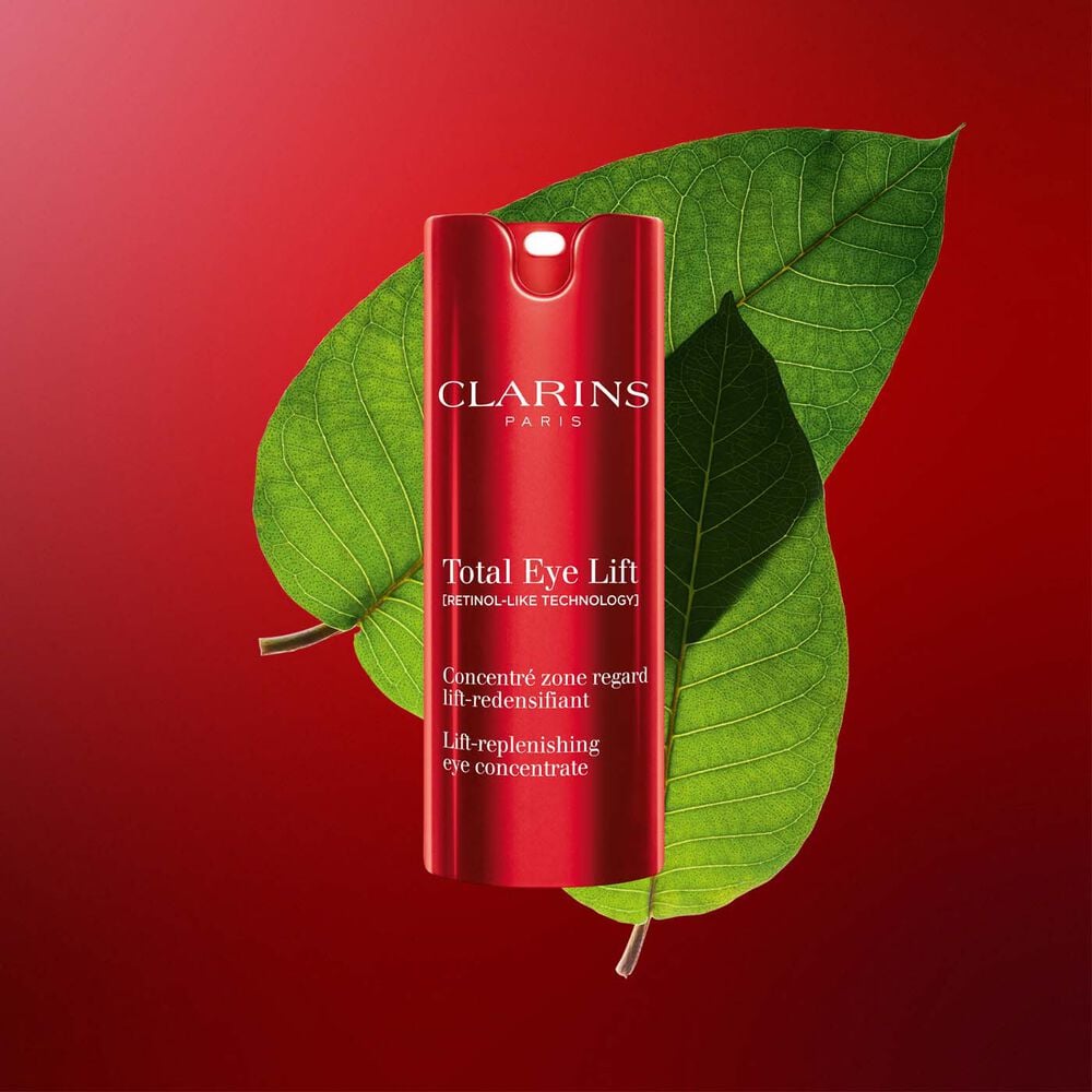 Packshot of Clarins Total Eye Lift anti-aging eye cream with harungana leaves on a dark red background.