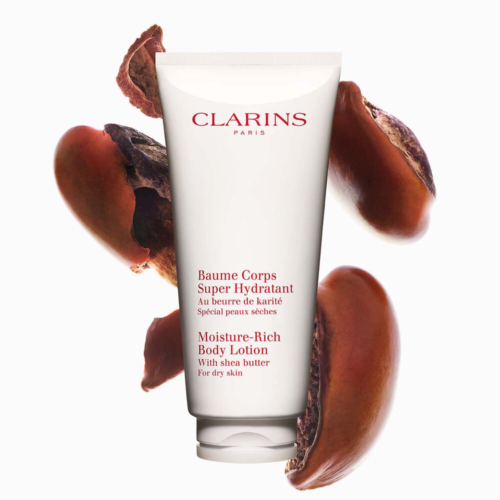 Packshot of a tube of Clarins Moisture-Rich Body Lotion by Clarins close to some shea nuts on a white background.