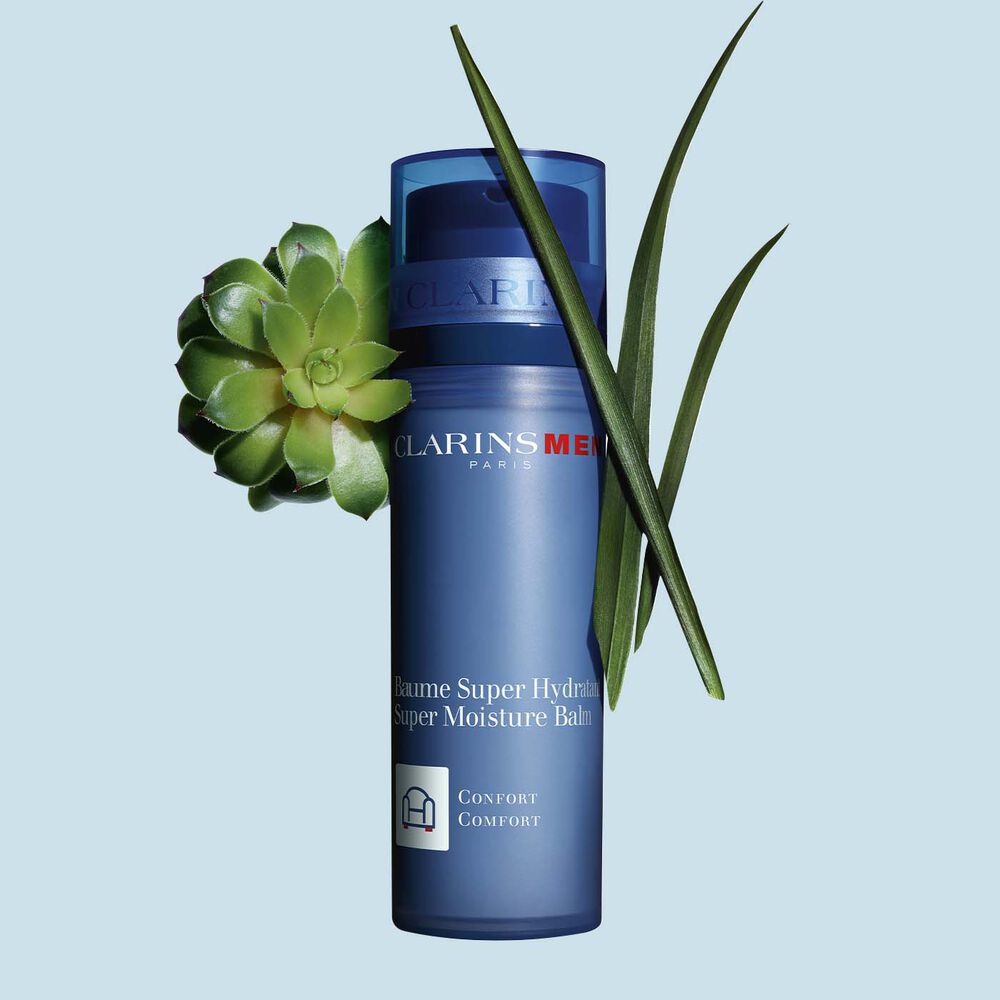 Packshot of a pump bottle of Clarins Men Super Moisture Balm close to gymnena and bison grass on a blue background.