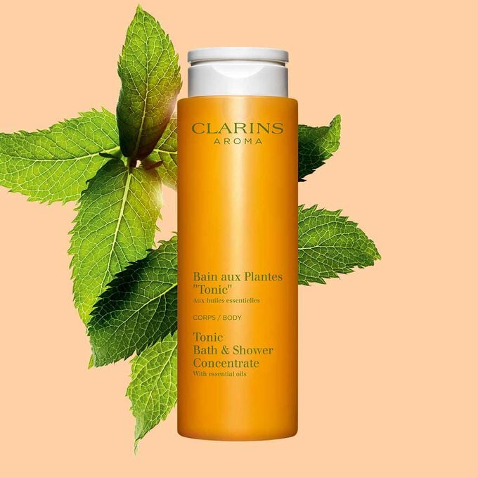Packshot of Clarins Tonic Bath and Shower Concentrate gel, close to some mint and rosemary leaves on an orange background.
