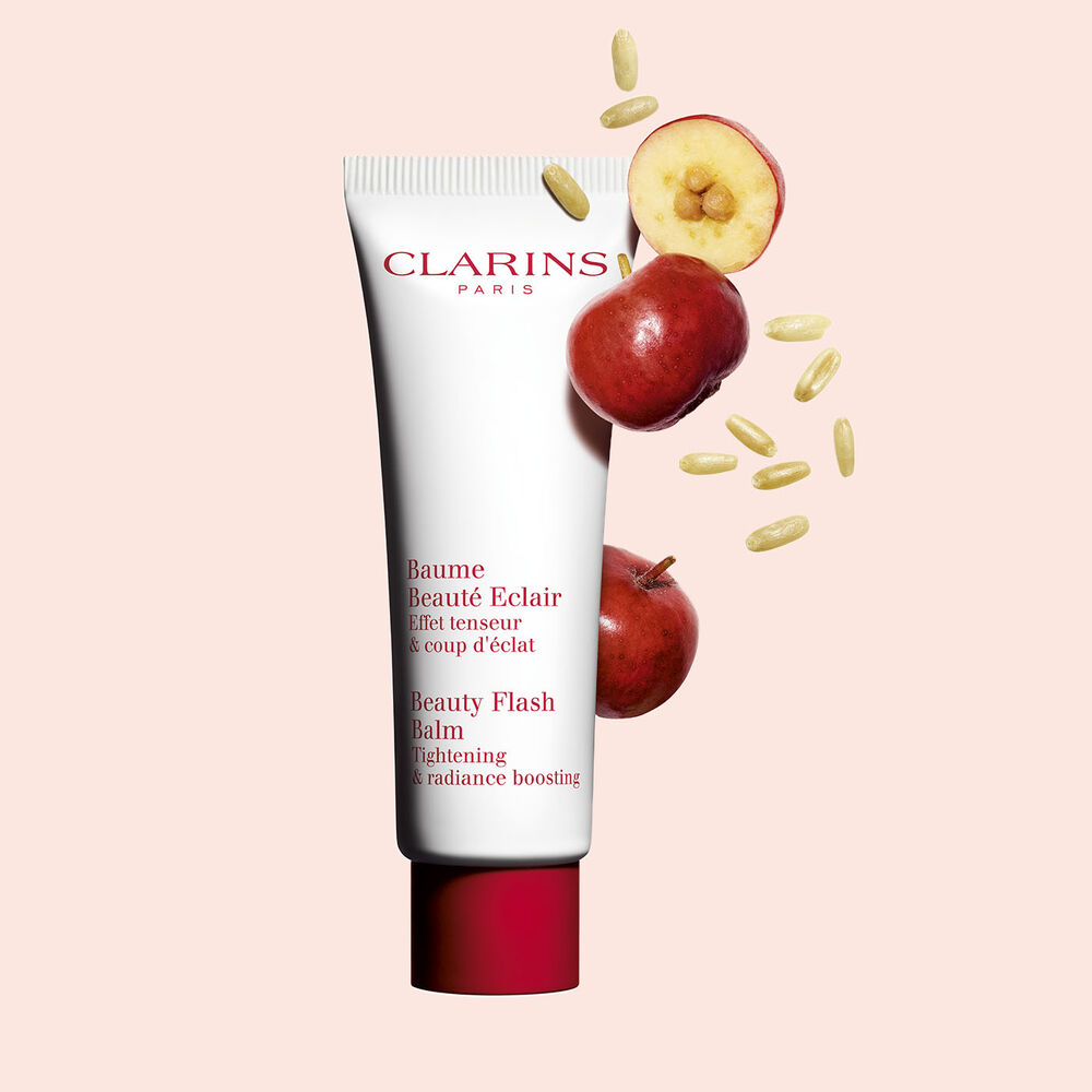 Packshot of a tube of Clarins Beauty Flash Balm close to acerola berries on a peach background.