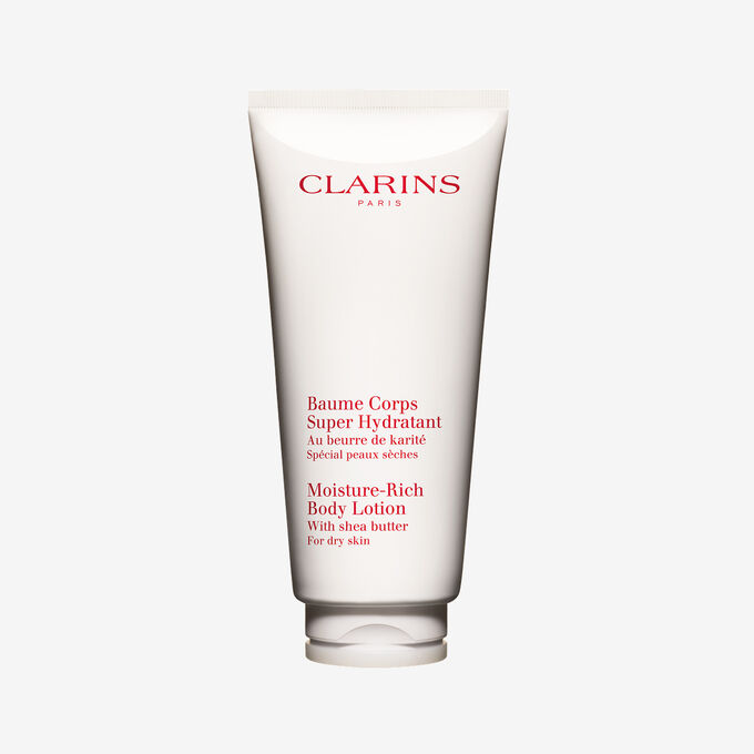 Packshot of a tube of Clarins Moisture-Rich Body Lotion by Clarins close to some shea nuts on a white background.