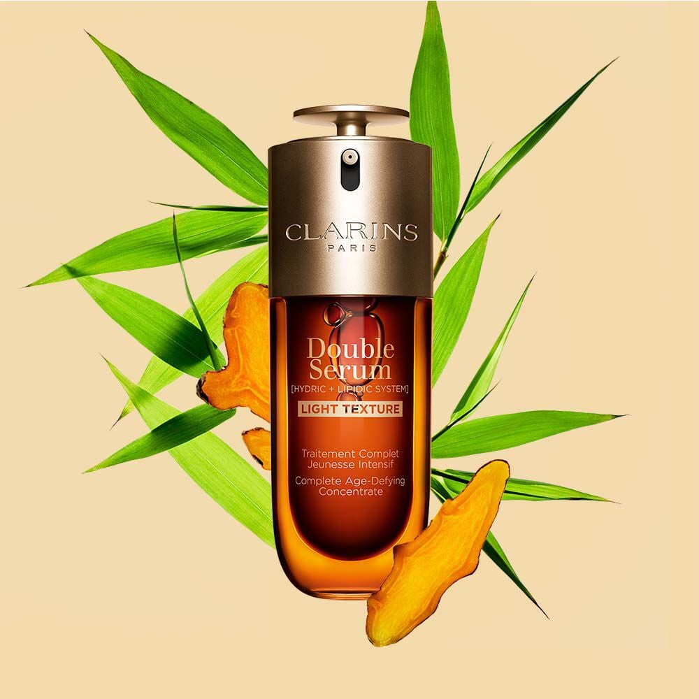 A 50ml bottle of Clarins Double Serum Light Texture among turmeric and provençal reed leaves against an orange background.