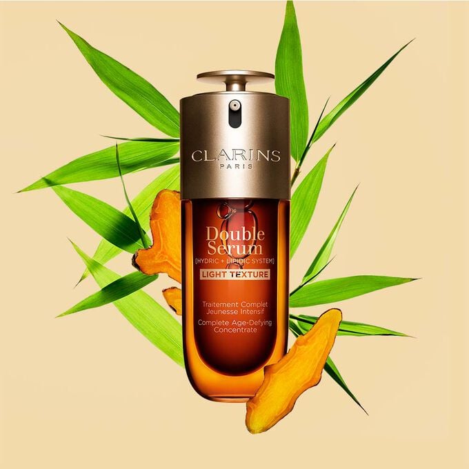 A 50ml bottle of Clarins Double Serum Light Texture among turmeric and provençal reed leaves against an orange background.