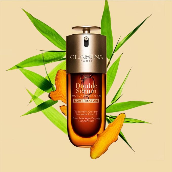 A 50ml bottle of Clarins Double Serum Light Texture among turmeric and provençal reed leaves against an orange background. A 50ml bottle of Clarins Double Serum Light Texture among turmeric and provençal reed leaves against an orange background.