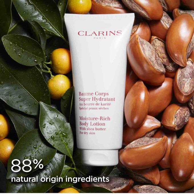 Clarins Moisture-Rich Body Lotion among orange tree leaves and shea nuts to illustrate the natural origin of the ingredients.
