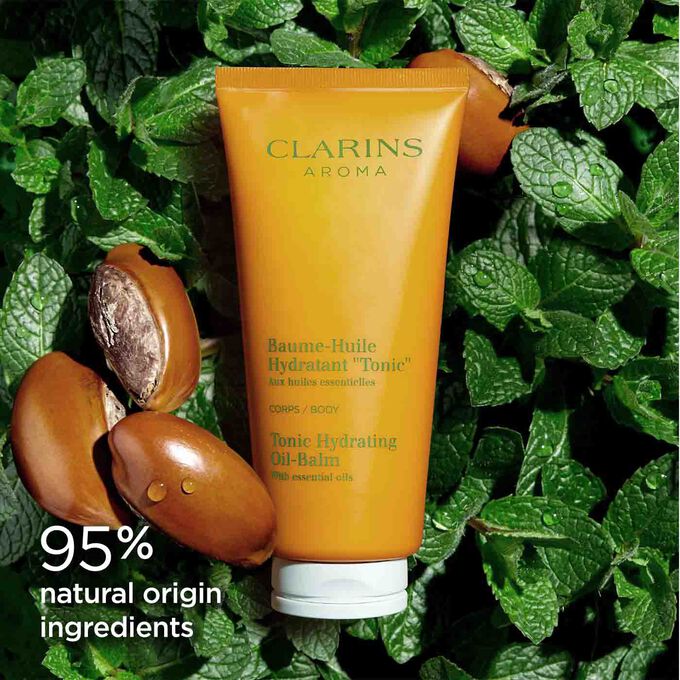 Tube of Clarins Tonic Hydrating Oil-balm among mint leaves and shea nuts to illustrate the natural origin of its ingredients.